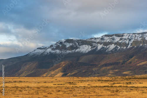gran cerro nevado con nubes nimbostrato oscuras en atardecer, con el sol de la tarde iluminando campos de colores dorados otoñales   photo