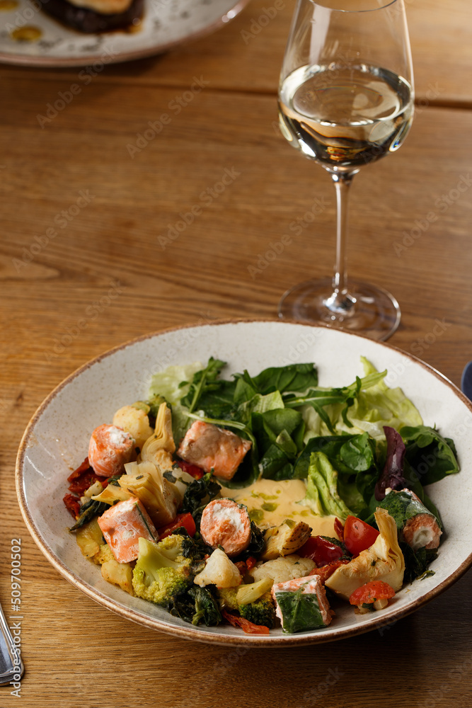 A salad with grilled salmon, mashed avocado and lettuce dressed with cream cheese. Close-up of the dish in a brown bowl isolated on brown background.