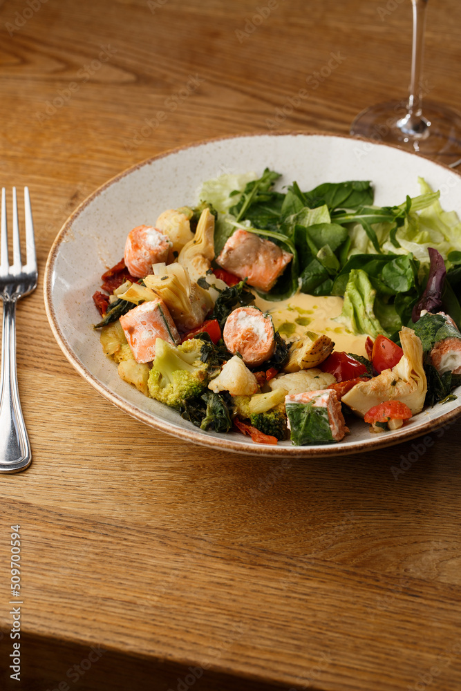 A salad with grilled salmon, mashed avocado and lettuce dressed with cream cheese. Close-up of the dish in a brown bowl isolated on brown background.