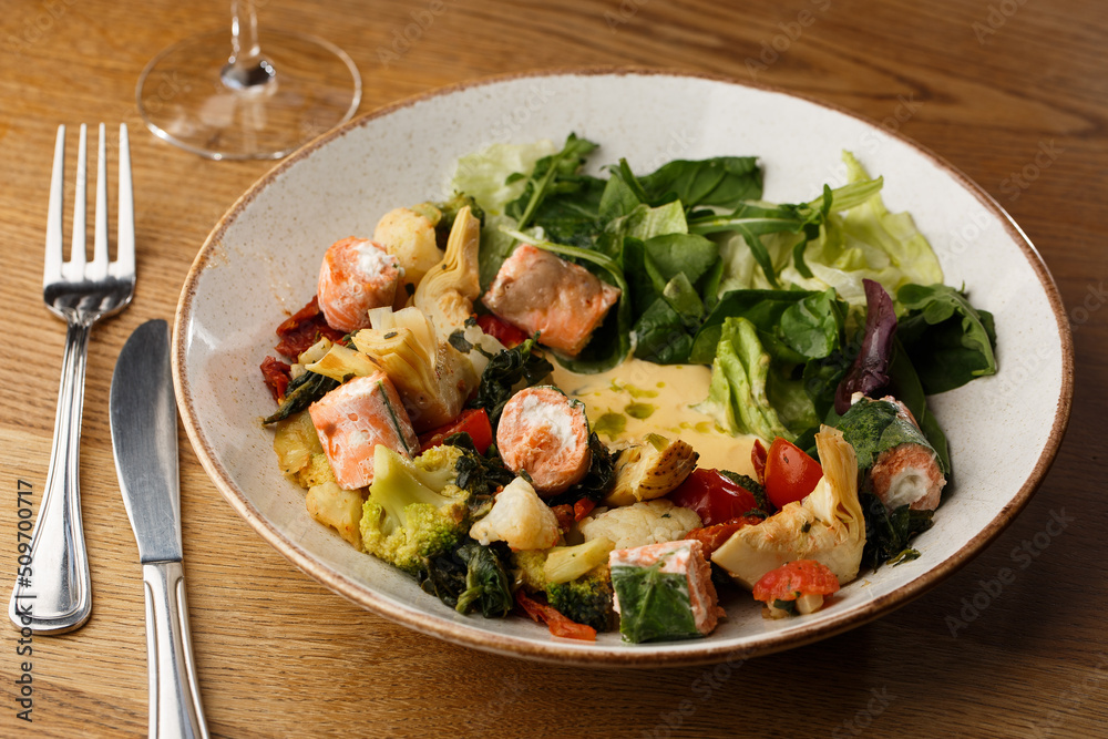 A salad with grilled salmon, mashed avocado and lettuce dressed with cream cheese. Close-up of the dish in a brown bowl isolated on brown background.