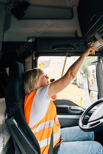 Middle age truck driver woman talking on radio and turns on tachograph, trucker occupation in Europe for females