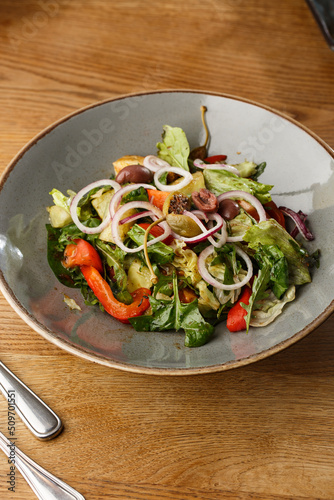 Obraz na płótnie Greek salad with fresh vegetables: tomato, cucumber, red bel pepper, lettuce, onion, olives and cheese. Close-up on a white round plate on a wooden background. Salad menu with ingredients w salonie