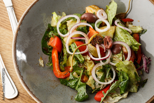 Greek salad with fresh vegetables: tomato, cucumber, red bel pepper, lettuce, onion, olives and cheese. Close-up on a white round plate on a wooden background. Salad menu with ingredients