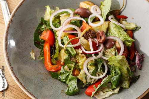 Obraz na płótnie Greek salad with fresh vegetables: tomato, cucumber, red bel pepper, lettuce, onion, olives and cheese. Close-up on a white round plate on a wooden background. Salad menu with ingredients w salonie