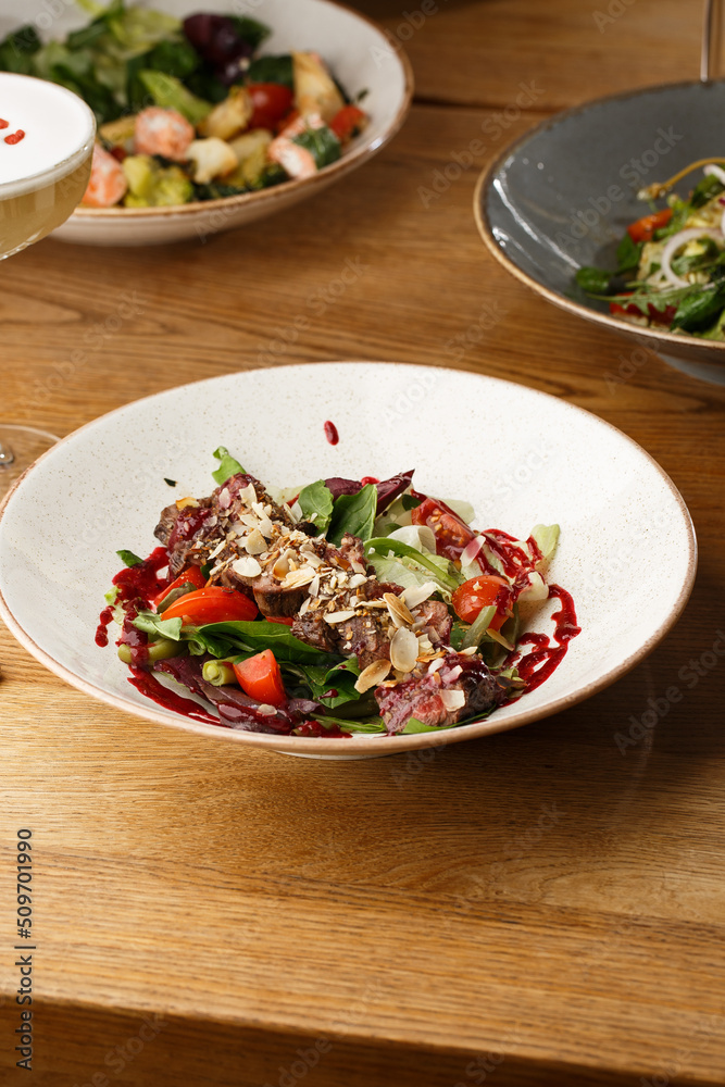 Salad with veal and tomatoes. Beef steak with raw vegetables mix side view. Grilled meat with garnish close-up. Delicious main course on table