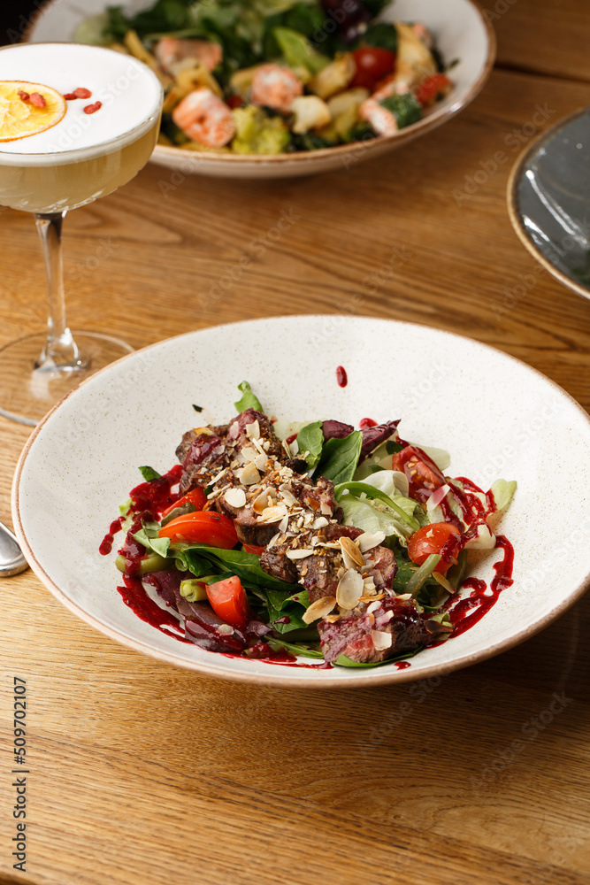 Salad with veal and tomatoes. Beef steak with raw vegetables mix side view. Grilled meat with garnish close-up. Delicious main course on table
