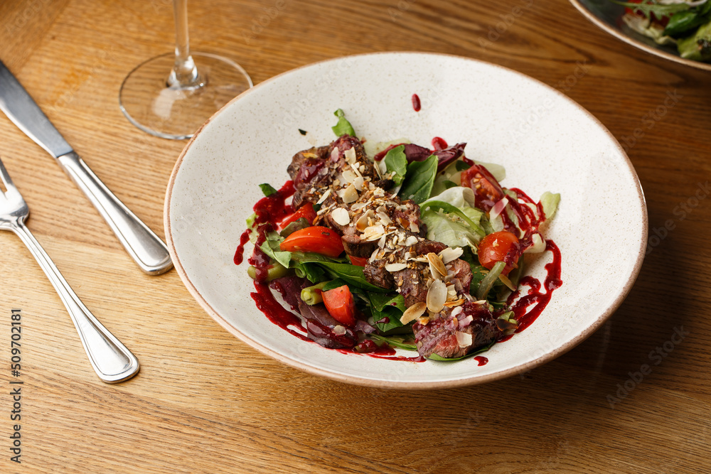 Salad with veal and tomatoes. Beef steak with raw vegetables mix side view. Grilled meat with garnish close-up. Delicious main course on table