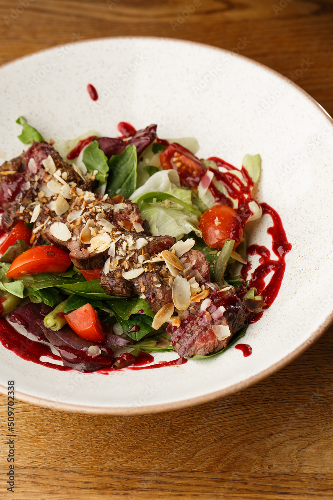 Salad with veal and tomatoes. Beef steak with raw vegetables mix side view. Grilled meat with garnish close-up. Delicious main course on table