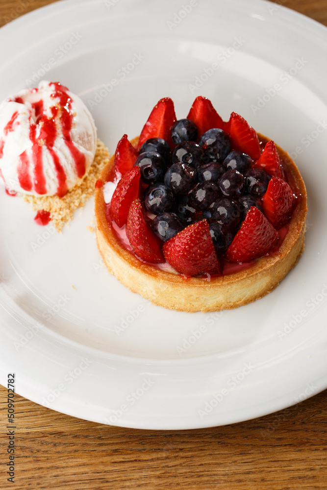 Berry tartlets with curd cream on a wooden background. Summer fruit baking. Tartlets with raspberries, blueberries and red currants. Served with ice cream.