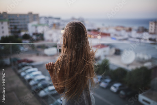 Girl with long hair stay on the balcony watch and dream. Summer time evening sunset, seaside.