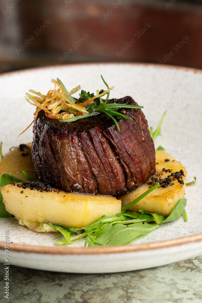 Grilled meat fillet steak medallion with green sauce, served with pear or apple. On dark background
