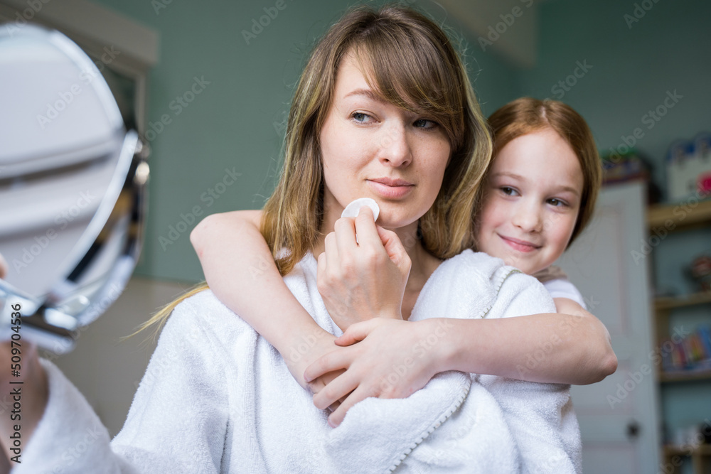 Attentive woman looking at the mirror and removing cosmetics with cotton pad Attentive woman looking at the mirror and removing cosmetics with cotton pad