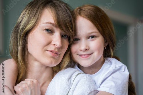 Lovely woman embracing with her little daughter while posing to the camera at the bathroom