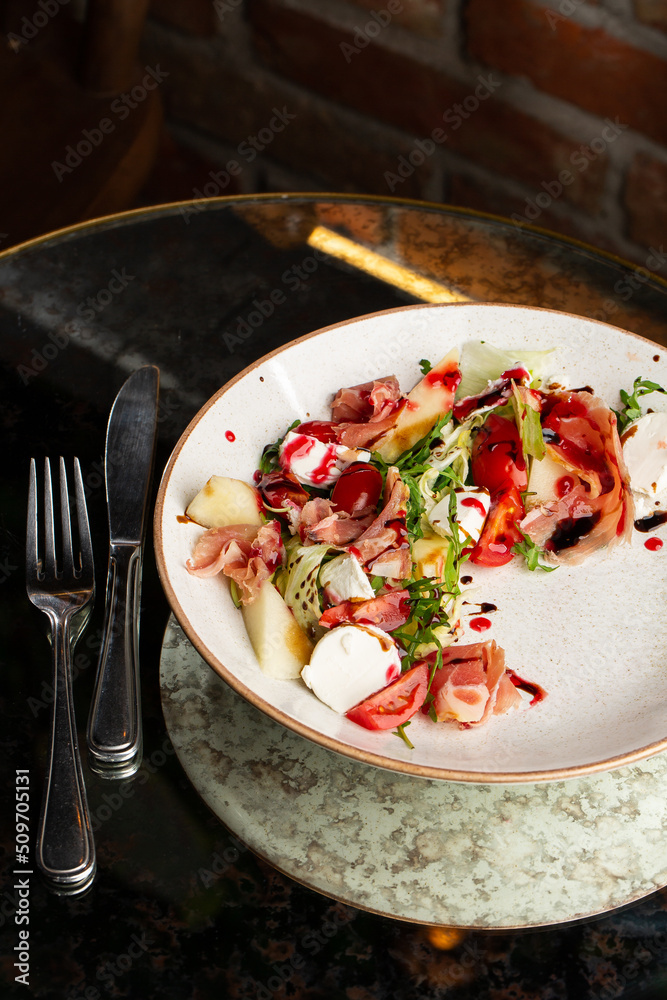Prosciutto crudo ham salad with mozzarella cheese and arugula on a plate. Bright background. Top view. Copy space