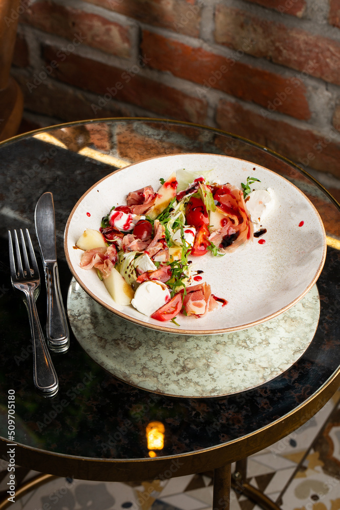 Prosciutto crudo ham salad with mozzarella cheese and arugula on a plate. Bright background. Top view. Copy space