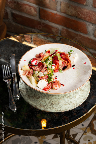 Prosciutto crudo ham salad with mozzarella cheese and arugula on a plate. Bright background. Top view. Copy space
