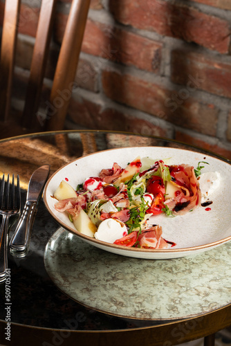 Obraz na płótnie Prosciutto crudo ham salad with mozzarella cheese and arugula on a plate. Bright background. Top view. Copy space w salonie