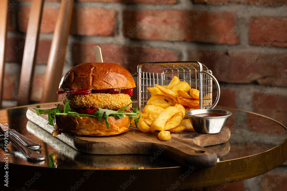 Big cheeseburger with french fries. Hamburger with beef patty onion, tomato, lettuce pickles, melted cheddar, mustards, tomato jam, mayo