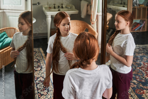 Red haired female child brushing her hair and preparing braids