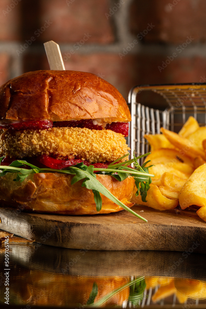 Big cheeseburger with french fries. Hamburger with beef patty onion, tomato, lettuce pickles, melted cheddar, mustards, tomato jam, mayo