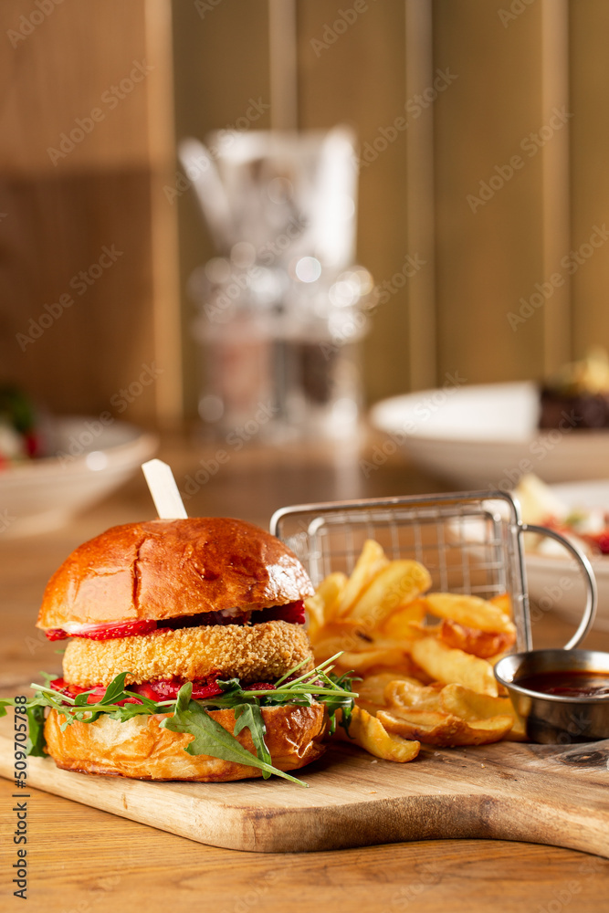Big cheeseburger with french fries. Hamburger with beef patty onion, tomato, lettuce pickles, melted cheddar, mustards, tomato jam, mayo