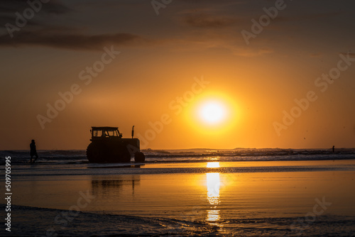 Silhouette of a tractor on the beach at sunset over the sea and reflection on the water © fotosdanielgbueno