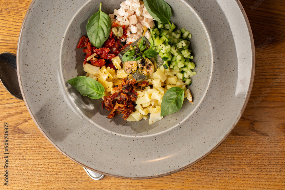 Closeup of cold soup okroshka with beef, vegetables and kefir served in a white bowl, selective focus. Summer, cold soup with cucumber, radish, egg, potatoes and fresh herbs seasoned with kefir.