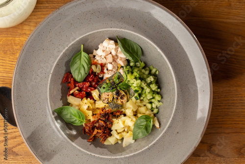 Obraz na płótnie Closeup of cold soup okroshka with beef, vegetables and kefir served in a white bowl, selective focus. Summer, cold soup with cucumber, radish, egg, potatoes and fresh herbs seasoned with kefir. w salonie