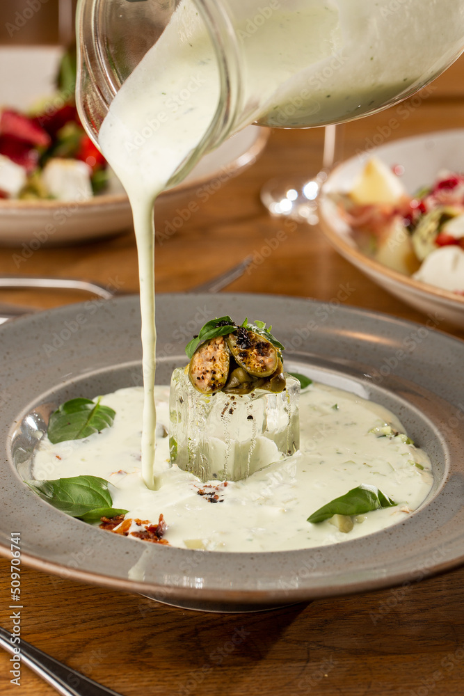 Closeup of cold soup okroshka with beef, vegetables and kefir served in a white bowl, selective focus. Summer, cold soup with cucumber, radish, egg, potatoes and fresh herbs seasoned with kefir.