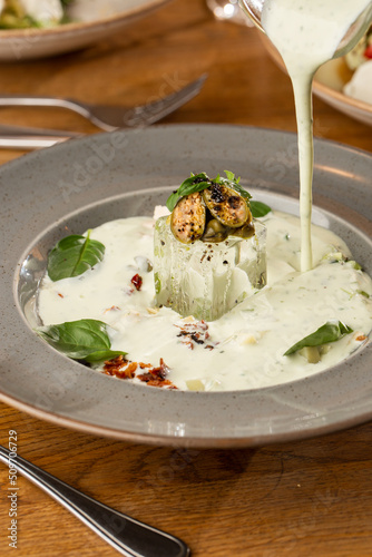 Closeup of cold soup okroshka with beef, vegetables and kefir served in a white bowl, selective focus. Summer, cold soup with cucumber, radish, egg, potatoes and fresh herbs seasoned with kefir.