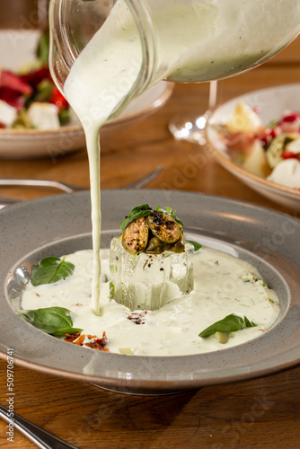 Obraz na płótnie Closeup of cold soup okroshka with beef, vegetables and kefir served in a white bowl, selective focus. Summer, cold soup with cucumber, radish, egg, potatoes and fresh herbs seasoned with kefir. w salonie
