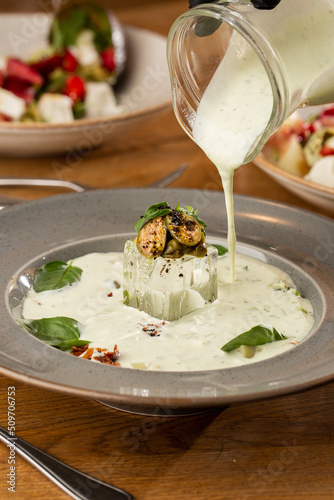 Obraz na płótnie Closeup of cold soup okroshka with beef, vegetables and kefir served in a white bowl, selective focus. Summer, cold soup with cucumber, radish, egg, potatoes and fresh herbs seasoned with kefir. w salonie