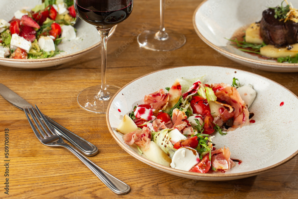 Prosciutto crudo ham salad with mozzarella cheese and arugula on a plate. Bright background. Top view. Copy space