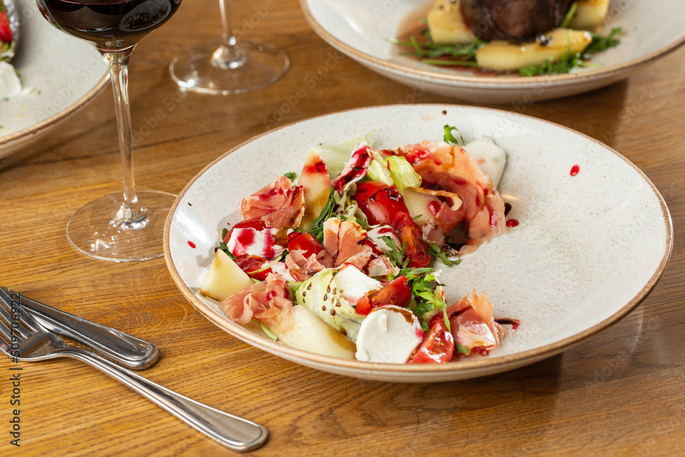 Prosciutto crudo ham salad with mozzarella cheese and arugula on a plate. Bright background. Top view. Copy space