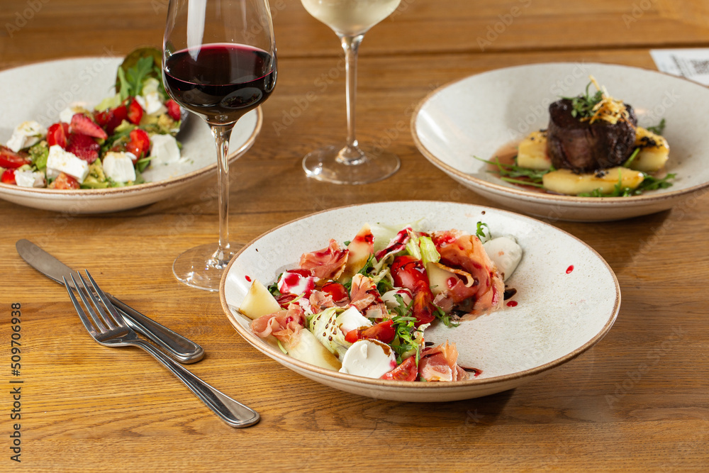 Prosciutto crudo ham salad with mozzarella cheese and arugula on a plate. Bright background. Top view. Copy space