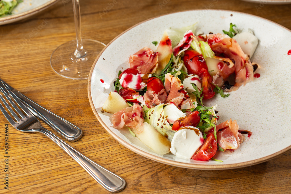 Prosciutto crudo ham salad with mozzarella cheese and arugula on a plate. Bright background. Top view. Copy space