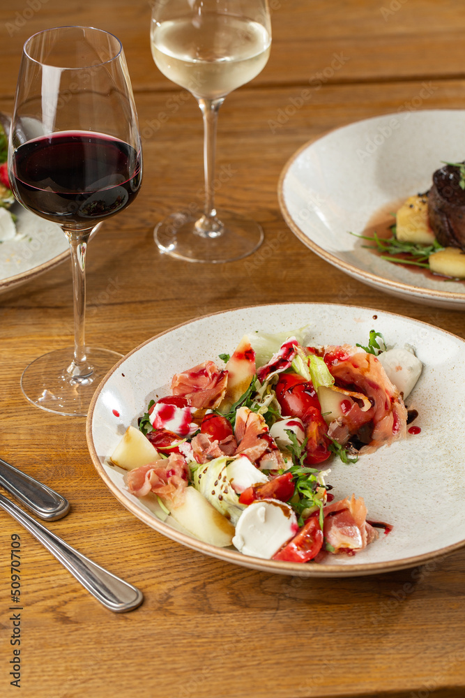 Prosciutto crudo ham salad with mozzarella cheese and arugula on a plate. Bright background. Top view. Copy space