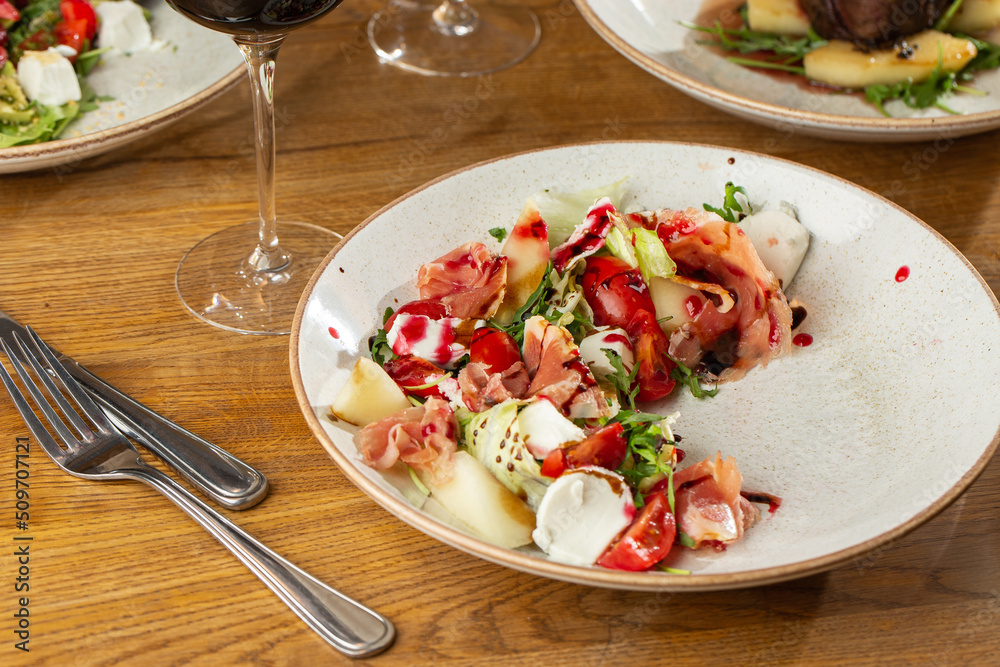 Prosciutto crudo ham salad with mozzarella cheese and arugula on a plate. Bright background. Top view. Copy space