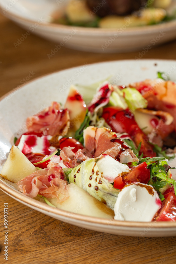 Prosciutto crudo ham salad with mozzarella cheese and arugula on a plate. Bright background. Top view. Copy space