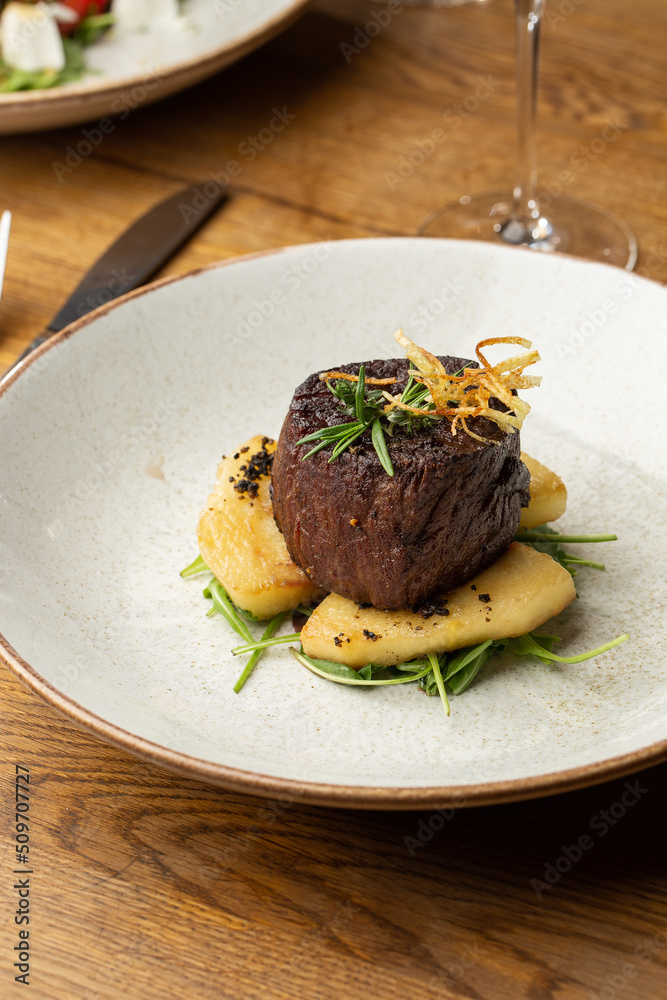Grilled meat fillet steak medallion with green sauce, served with pear or apple. On dark background