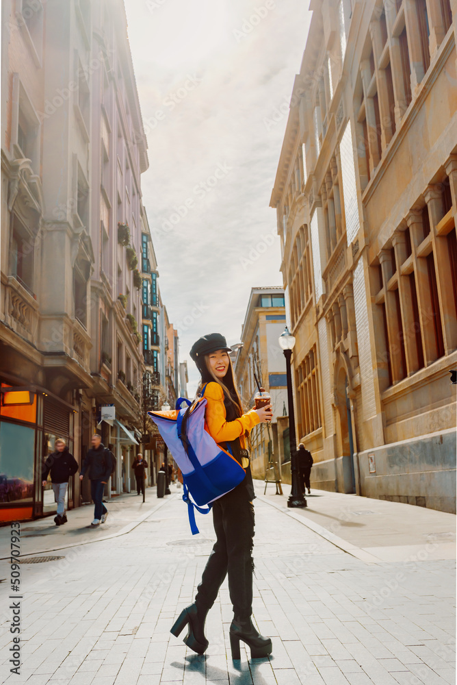 Asian young woman with backpack sightseeing in a European city while having a special coffee.