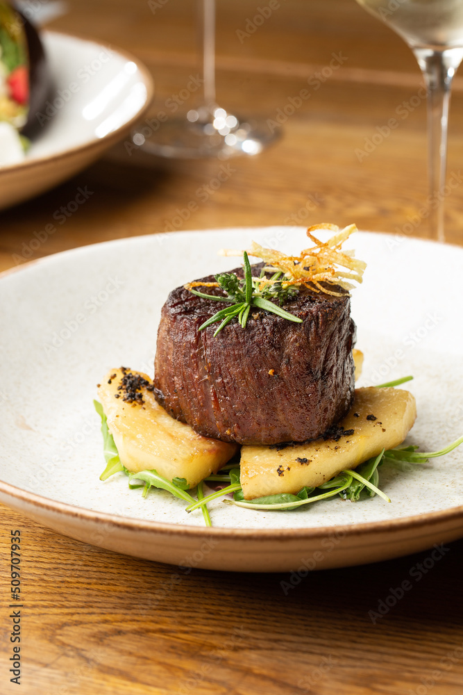 Grilled meat fillet steak medallion with green sauce, served with pear or apple. On dark background