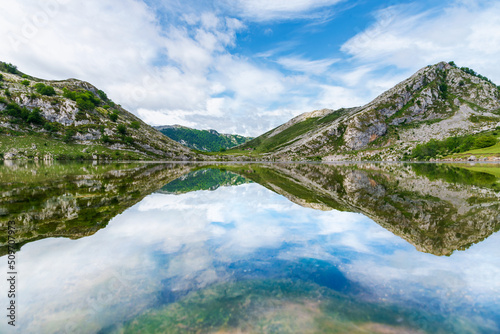 Lakes of Covadonga, Lake Enol, with the mountains and clouds reflected on the water, on a day with a cloudy sky and no wind.
