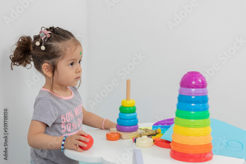 Little girl sitting at a table with toys, crayons and drawing sheets, with copy space