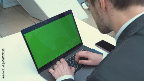 Over the shoulder shot of a businessman typing on laptop and looking at green screen. Office person using computer, chromo key display photo