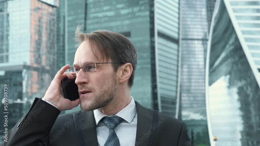 Handsome businessman leader executive boss talking with business partner on mobile phone. Busy business corporate concept Skyscrapers on background. Handsome businessman leader executive boss talking with business partner on mobile phone. Busy business corporate concept Skyscrapers on background.