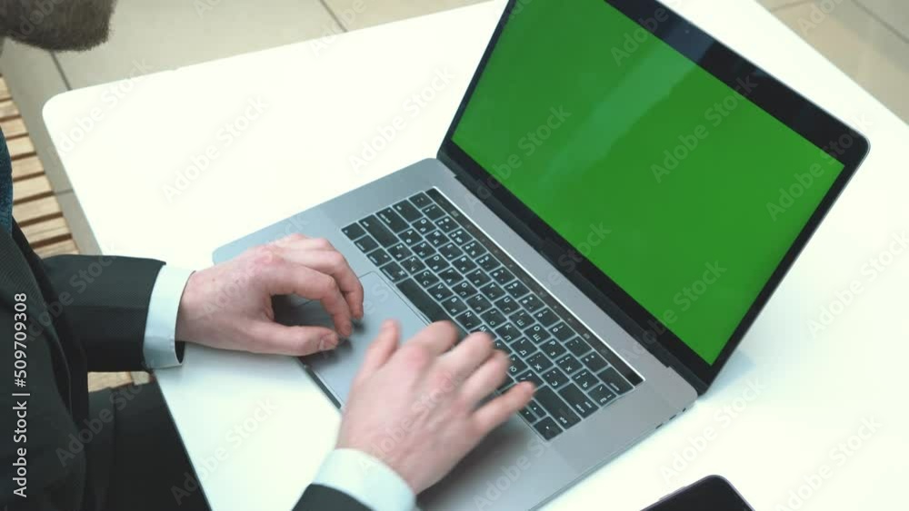 Over the shoulder shot of a businessman typing on laptop and looking at green screen. Office person using computer, chromo key display Over the shoulder shot of a businessman typing on laptop and looking at green screen. Office person using computer, chromo key display