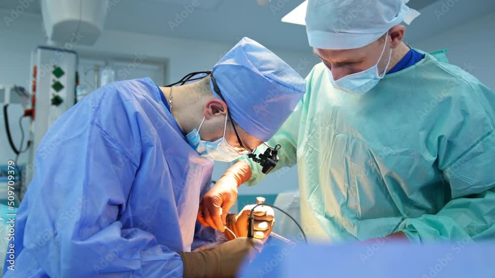 Hard-working surgeon at operation using tools bending over the patient. Male assistant helping the doctor. Hard-working surgeon at operation using tools bending over the patient. Male assistant helping the doctor.