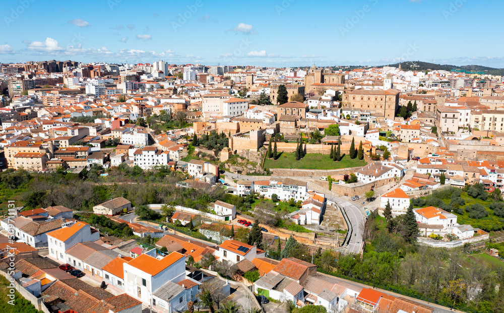 Aerial view of Caceres cityscape overlooking brownish tiled roofs of historic quarter against backdrop of modern high-rise buildings in spring day, Extremadura, Spain