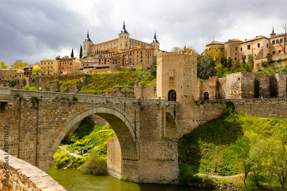Picturesque view of Alcazar fortress and Alcantara bridge over Tagus river at old Spanish town of Toledo - obrazy, fototapety, plakaty 